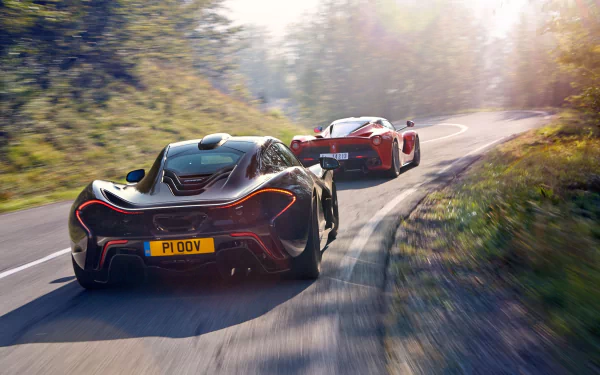 A stunning HD desktop wallpaper featuring a black McLaren P1 and a Ferrari LaFerrari racing on a scenic, winding road. The sunlit backdrop enhances the sleek design and dynamic presence of these supercars.
