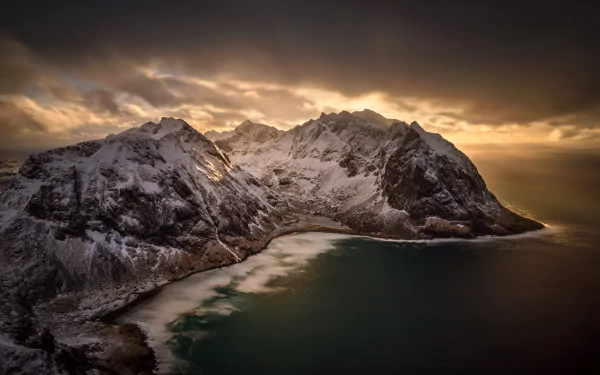 A stunning HD desktop wallpaper of the Lofoten archipelago, showcasing snow-covered mountains bathed in dramatic sunlight against a serene coastal landscape.