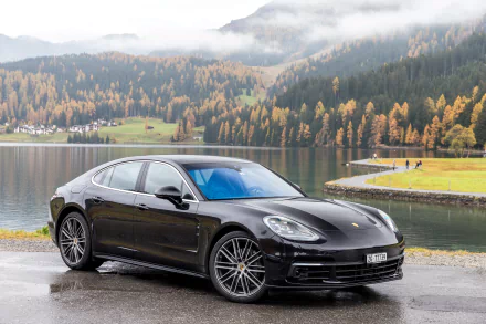 Black Porsche Panamera 4S parked by a lakeside with autumn trees and misty mountains in the background, captured as an HD desktop wallpaper.