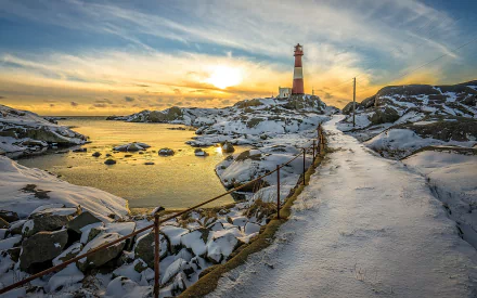 HD desktop wallpaper of a snowy walkway leading to a man-made lighthouse, with an ocean view at sunset.