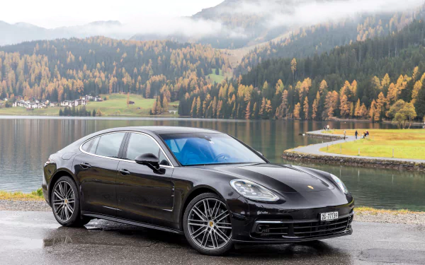 Black Porsche Panamera 4S parked by a lakeside with autumn trees and misty mountains in the background, captured as an HD desktop wallpaper.