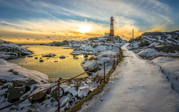 HD desktop wallpaper of a snowy walkway leading to a man-made lighthouse, with an ocean view at sunset.
