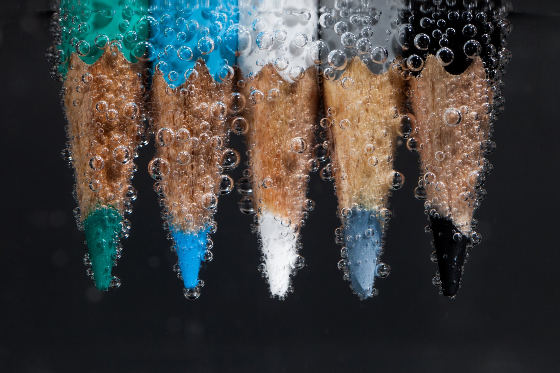 Macro photography of five colored pencil tips (teal, blue, white, gray, black) cloaked in water bubbles on a black backdrop, vivid colors — 4K Ultra HD PC desktop wallpaper and background.