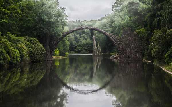 Devil's Bridge arching over a calm river, surrounded by lush greenery, with its reflection creating a near-perfect circle in this HD nature and man-made bridge wallpaper.