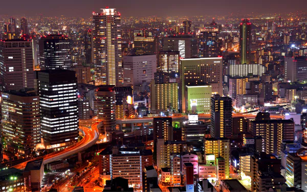 Nighttime cityscape of Osaka, Japan, featuring illuminated skyscrapers and buildings with vibrant city lights spreading across the urban skyline.