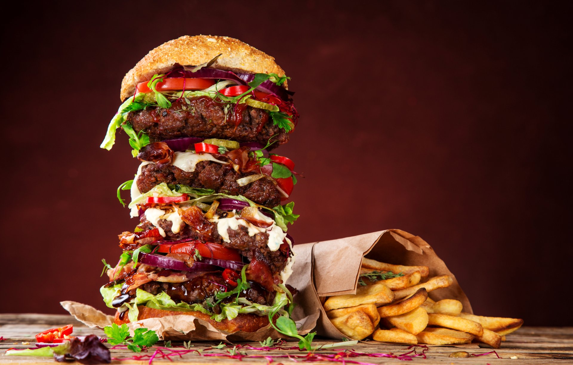 A towering, juicy burger stacked with fresh lettuce, tomatoes, and melted cheese, accompanied by crispy French fries, presented as a vibrant 4K Ultra HD desktop wallpaper.