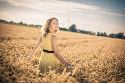 A blonde woman in a yellow dress stands in a wheat field during summer, with a blurred background enhancing the mood. The image is a high-definition desktop wallpaper and background.