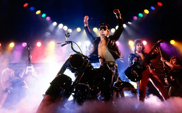 HD PC desktop wallpaper: Judas Priest–inspired heavy metal band onstage, leather‑clad singer on a motorcycle amid fog, guitars and vivid multicolored spotlights.