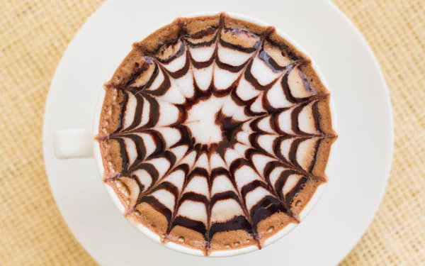 Top view of a coffee cup with intricate chocolate web design on frothy surface, captured in 4K Ultra HD as a desktop wallpaper and background.
