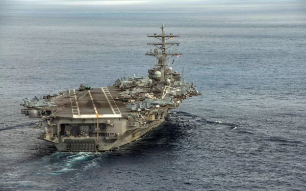 Aerial view of the USS Ronald Reagan (CVN-76), a military aircraft carrier, navigating through calm waters, showcasing its impressive structure and operational readiness.