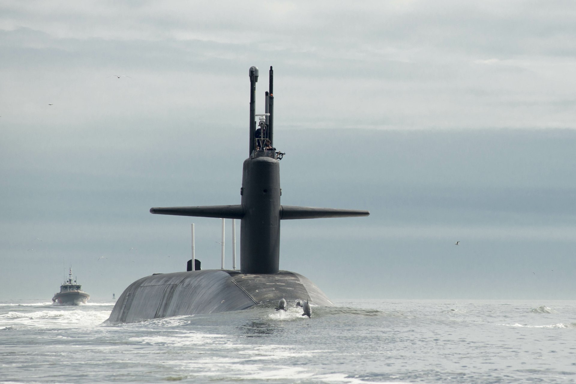 4K Ultra HD image of the USS Tennessee (SSBN-734) submarine surfacing in the ocean with a dolphin nearby, representing the United States Navy and military strength.