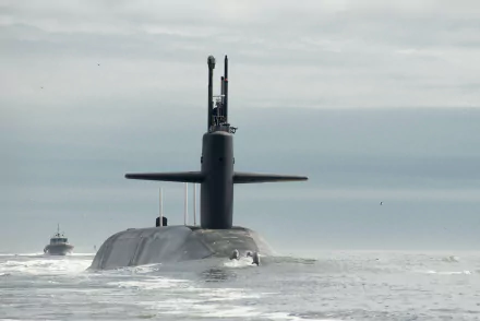 4K Ultra HD image of the USS Tennessee (SSBN-734) submarine surfacing in the ocean with a dolphin nearby, representing the United States Navy and military strength.