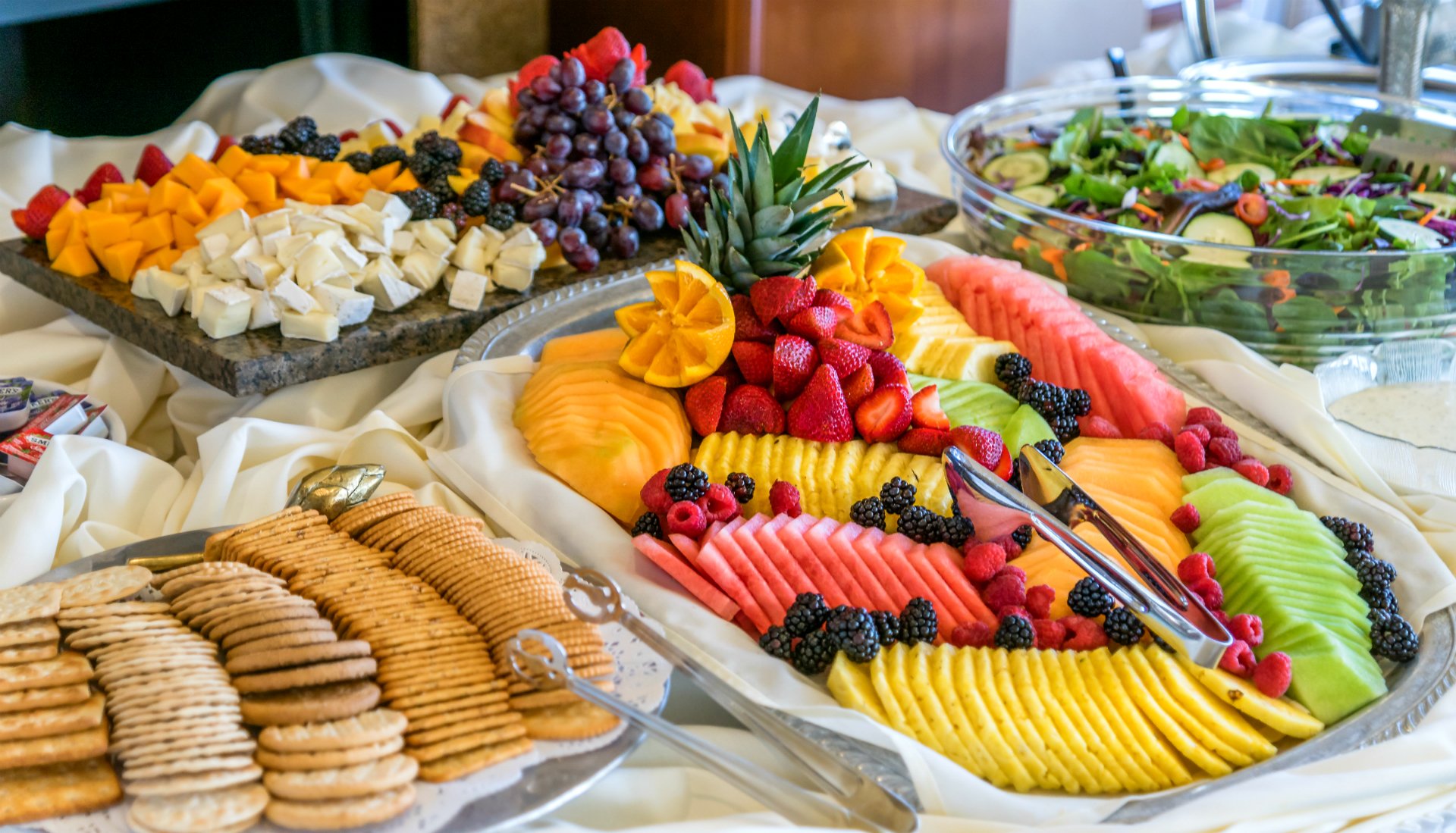 A vibrant HD wallpaper featuring a lavish spread of assorted fruits including strawberries, blackberries, grapes, pineapple, mango, raspberries, kiwi, and watermelon, accompanied by cheese, salad, and biscuits.