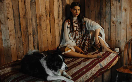 An HD desktop wallpaper featuring a brunette model with lipstick, relaxing on a wooden bench beside a dog. The rustic background adds to the cozy atmosphere.