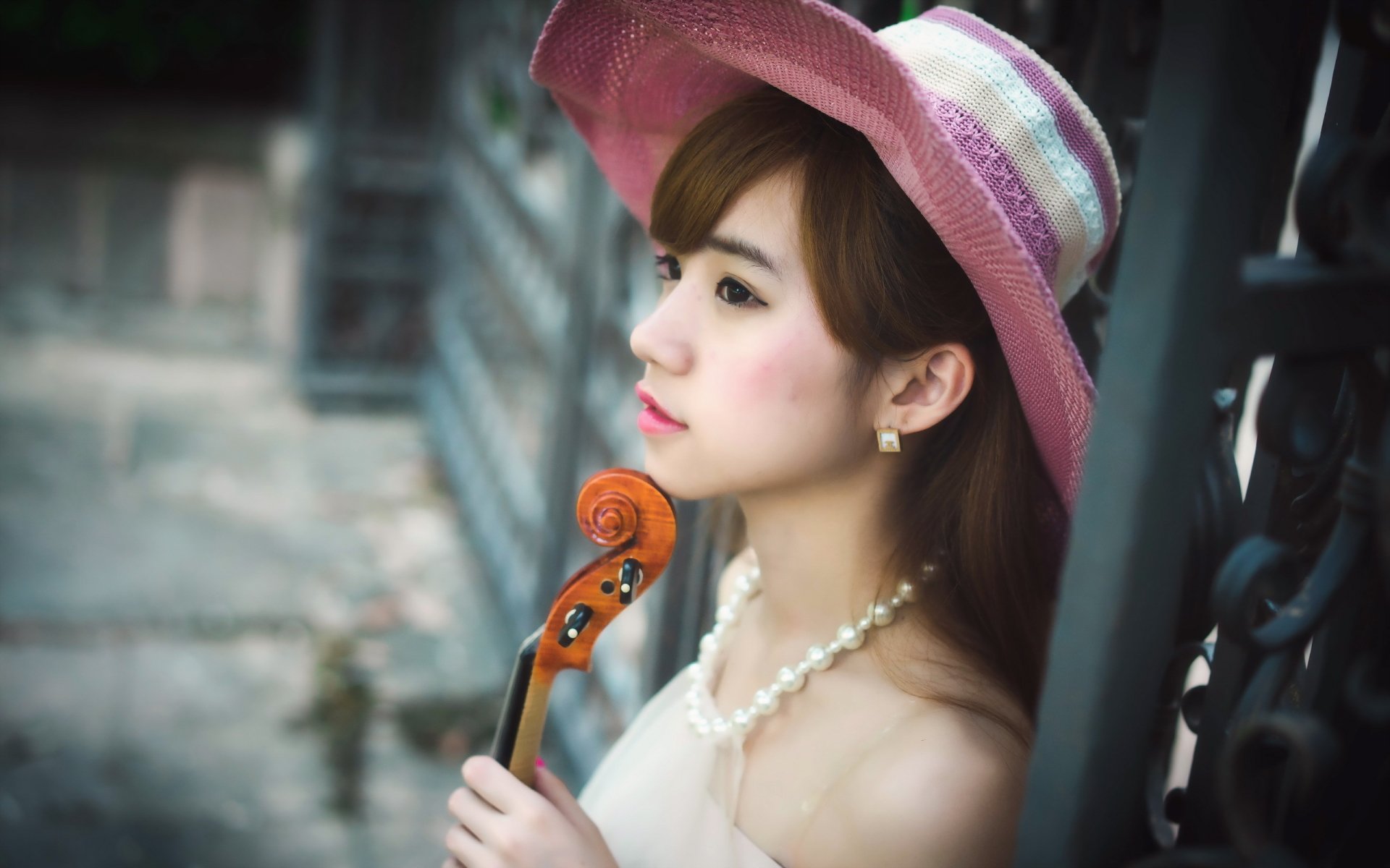 HD desktop wallpaper of an Asian brunette woman with brown eyes wearing a pink hat, holding a violin, and gazing thoughtfully to the side.