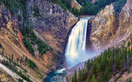 Stunning HD desktop wallpaper of a majestic waterfall cascading down a cliff into a serene river, surrounded by lush greenery in Yellowstone National Park.