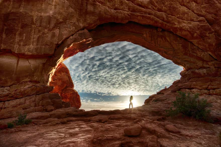A person stands beneath a large natural rock arch at Arches National Park, captured in stunning detail for a 4K Ultra HD desktop wallpaper.