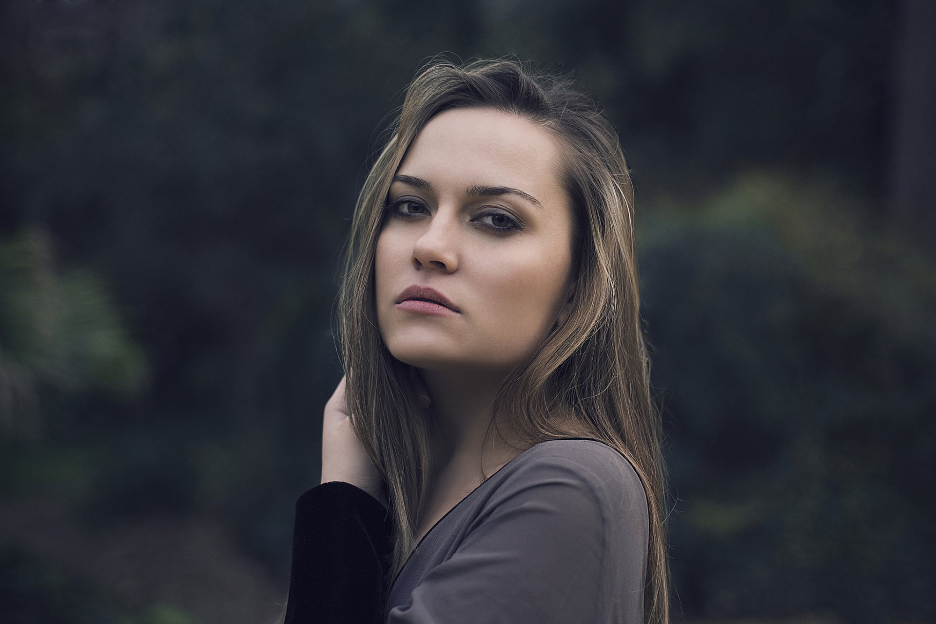 HD desktop wallpaper of a brunette woman model with long hair, posing outdoors against a blurred natural background.