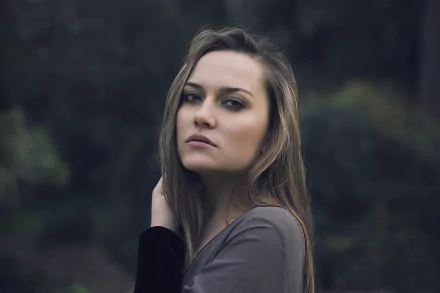 HD desktop wallpaper of a brunette woman model with long hair, posing outdoors against a blurred natural background.