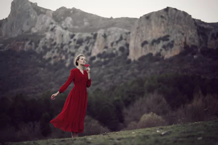 Moody HD desktop wallpaper: a woman model in a flowing red dress stands against a blurred mountain landscape, dramatic depth of field emphasizing her solitary, contemplative pose.