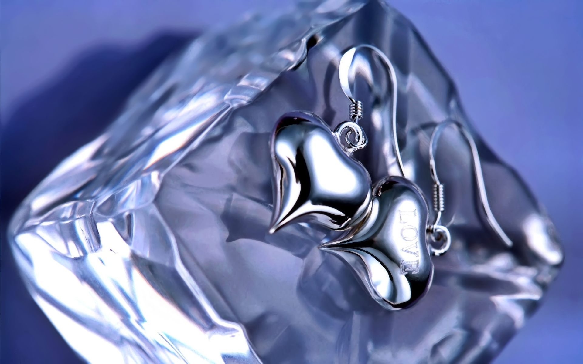 HD PC desktop wallpaper of silver heart earrings resting on an ice-like crystal, artistic cool-blue background.