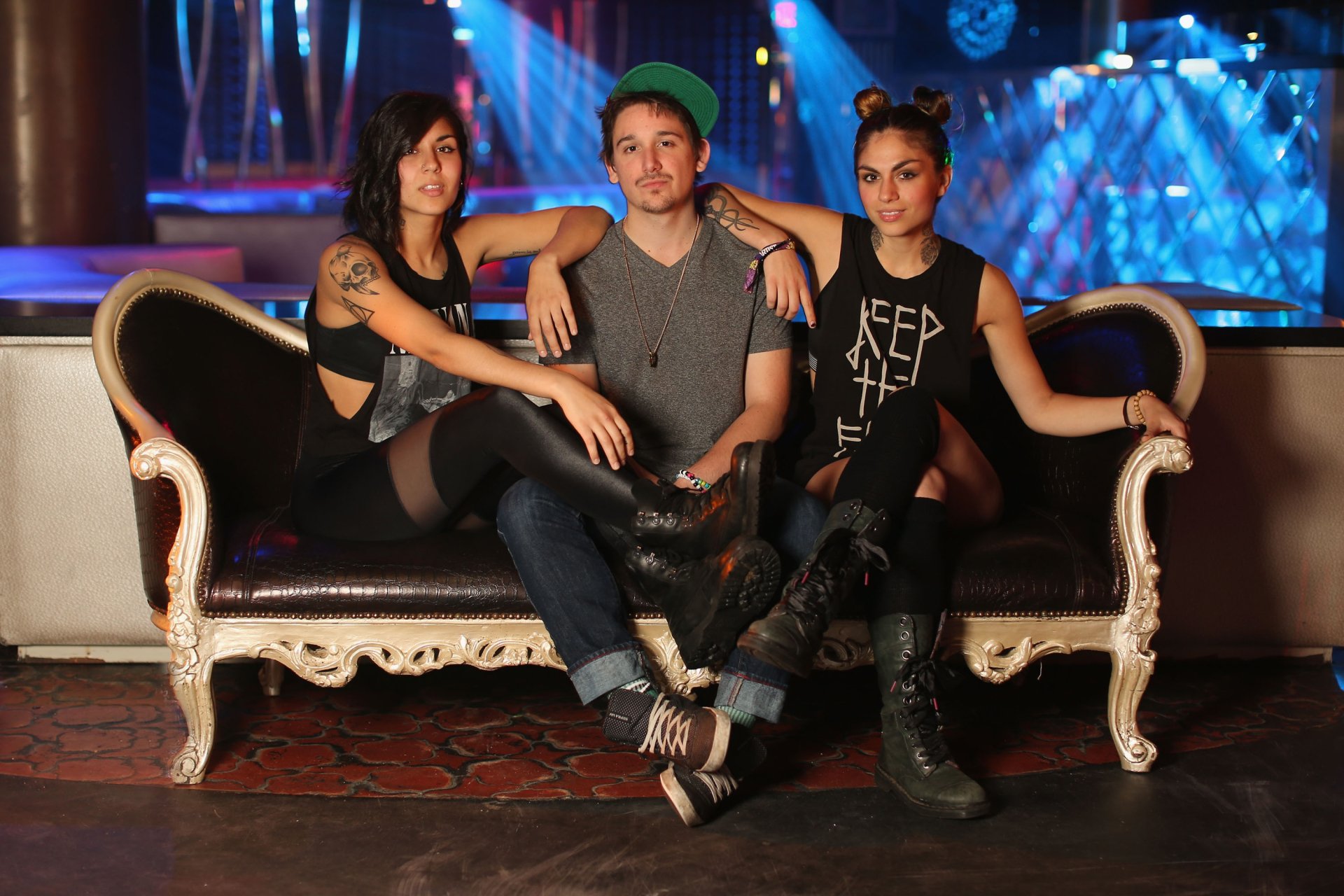 HD PC desktop wallpaper featuring the music group Krewella posing on an ornate black sofa with vibrant stage lights in the background.