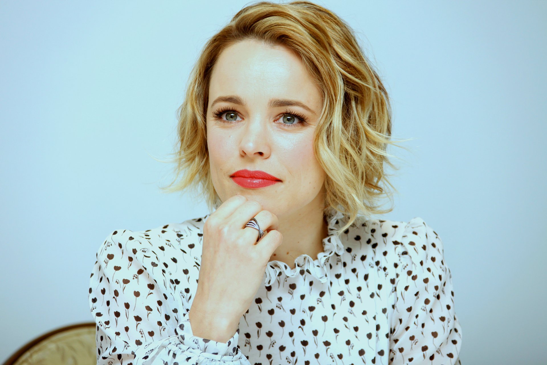 HD desktop wallpaper of Canadian actress Rachel McAdams with short blonde hair, wearing a white patterned blouse, against a light background.