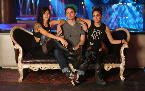 HD PC desktop wallpaper featuring the music group Krewella posing on an ornate black sofa with vibrant stage lights in the background.