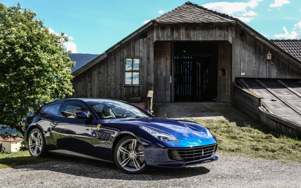 A sleek blue Ferrari GTC4Lusso grand tourer parked in front of a rustic wooden barn, captured in a high-resolution 4K Ultra HD desktop wallpaper.