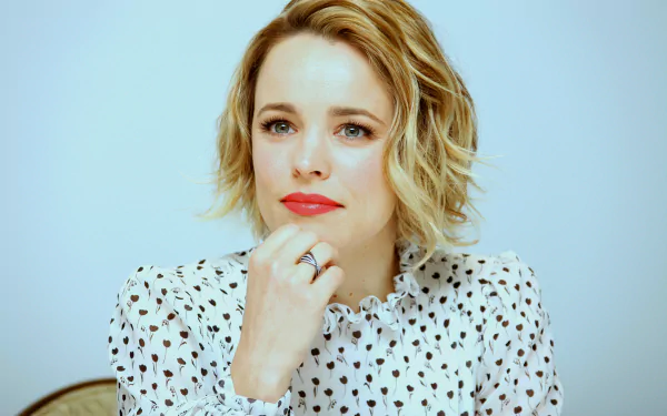 HD desktop wallpaper of Canadian actress Rachel McAdams with short blonde hair, wearing a white patterned blouse, against a light background.