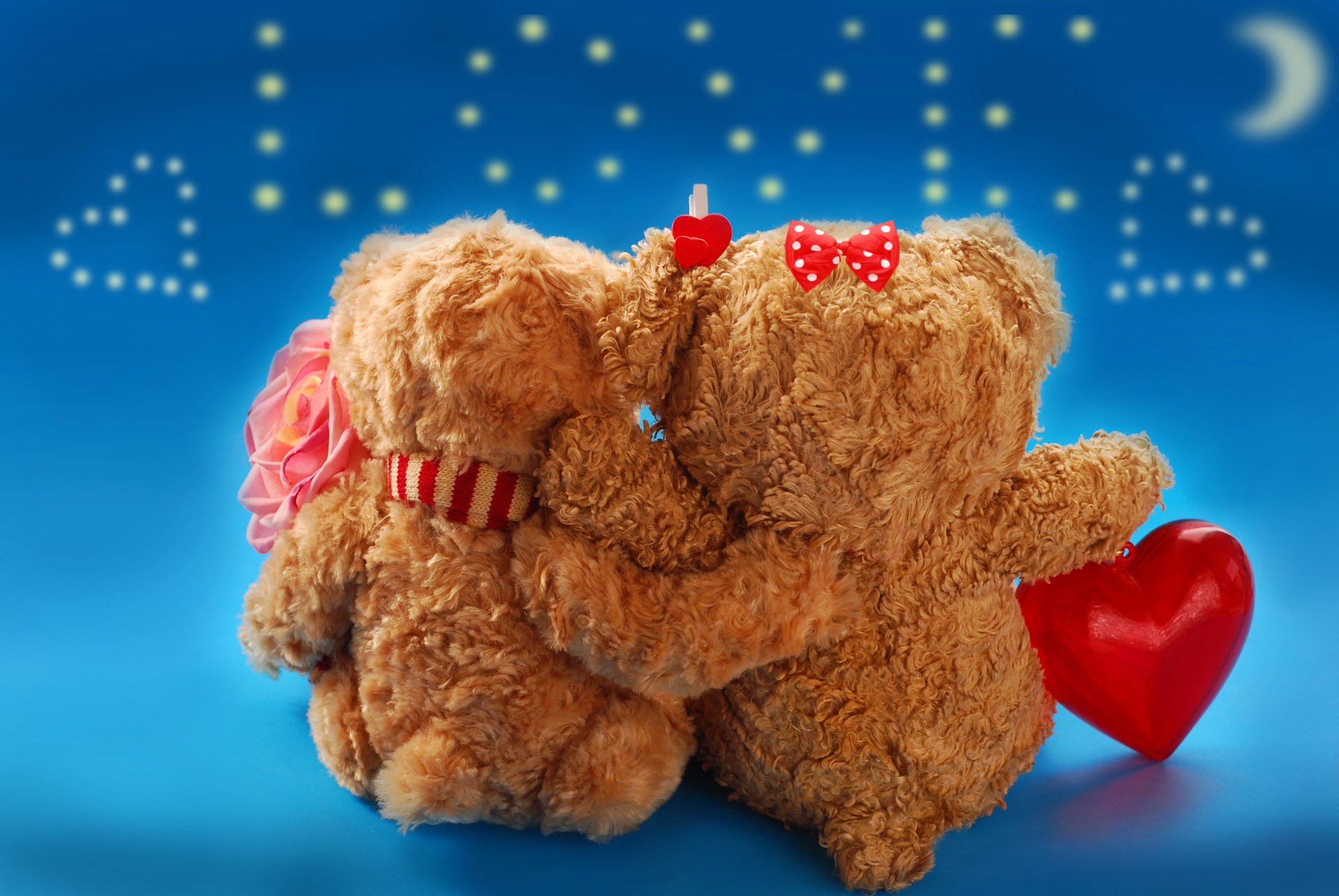 Two teddy bears hug with LOVE and hearts in the background. They are sitting on a blue surface with a heart-shaped object in their paws, depicting a romantic Valentine's Day scene.