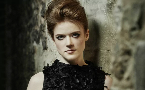HD desktop wallpaper featuring Rose Leslie, a redhead actress, posing against a textured stone wall in a black textured dress.
