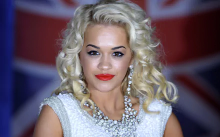 A striking HD desktop wallpaper featuring English singer Rita Ora with blonde hair, red lipstick, earrings, and a necklace, set against a background with British flag elements.