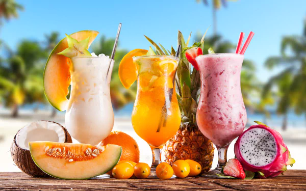 Tropical fruit drinks in glasses, surrounded by coconut, melon, pineapple, and pitaya, set against a sunny beach backdrop. HD desktop wallpaper.