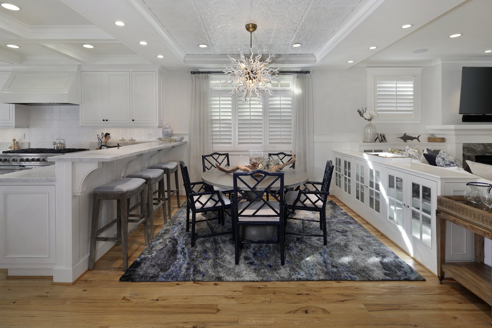 Modern kitchen and dining room featuring white cabinetry, a central dining table with black chairs, bar stools, and stylish lighting, captured in 4K Ultra HD.
