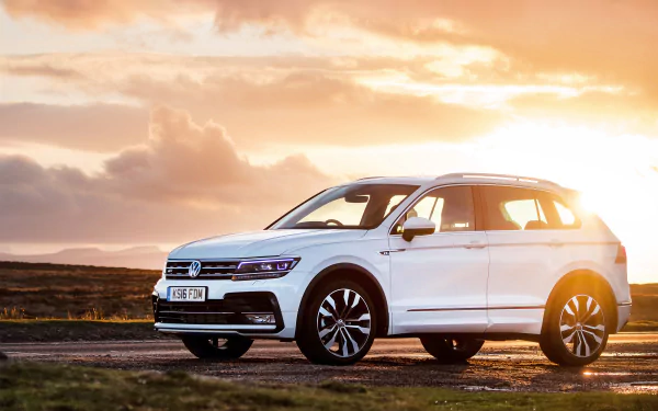 White Volkswagen Tiguan SUV parked on a road during a vibrant sunset, captured in high-definition for a PC desktop wallpaper background.