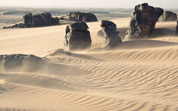 Wind sweeps across sand dunes and rock formations in the Sahara Desert at Tassili N'Ajjer, Algeria, showcasing the vast, natural landscape of Africa in 4K Ultra HD.