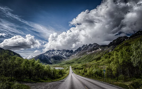 HD desktop wallpaper featuring a road cutting through lush green valleys with towering mountains under a dramatic cloudy sky in a stunning landscape setting.