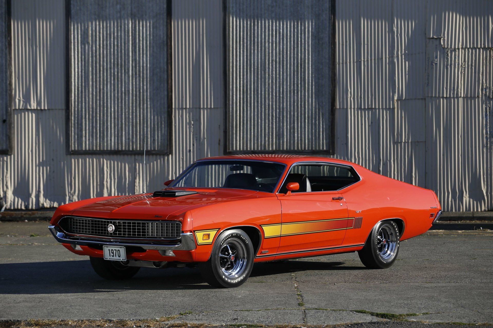 5K Ultra HD PC desktop wallpaper of an orange Ford Torino Cobra/GT muscle car parked before a corrugated metal wall, showcasing classic 1970s styling and bold racing stripes.