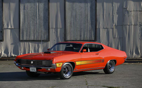 5K Ultra HD PC desktop wallpaper of an orange Ford Torino Cobra/GT muscle car parked before a corrugated metal wall, showcasing classic 1970s styling and bold racing stripes.