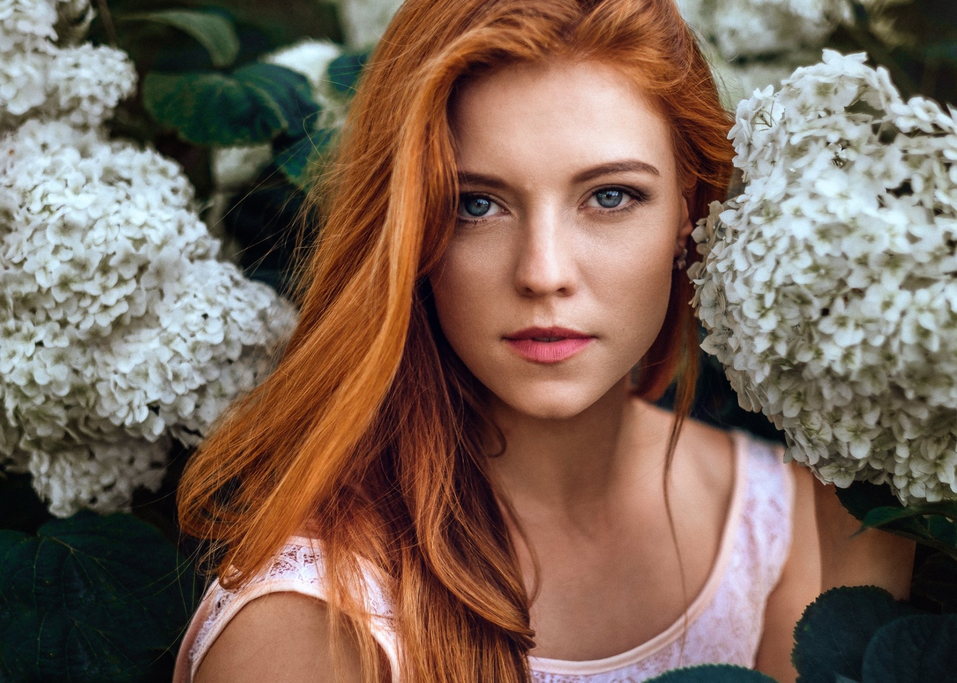 A redheaded woman with blue eyes poses amidst white flowers, showcasing her serene expression. This high-definition image serves as a captivating desktop wallpaper.
