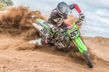 A motocross rider on a green motorcycle kicks up dirt while racing through a sandy track, captured in this HD desktop wallpaper showcasing intense off-road sports action.