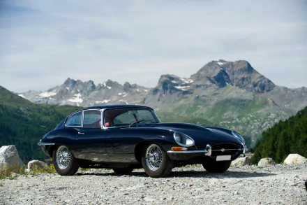 A sleek black Jaguar E-Type supercar parked on a rocky mountain road with towering peaks in the background, captured in stunning 4K Ultra HD.