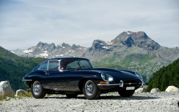 A sleek black Jaguar E-Type supercar parked on a rocky mountain road with towering peaks in the background, captured in stunning 4K Ultra HD.