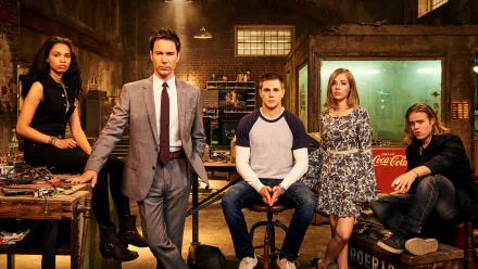 HD desktop wallpaper: five characters from the TV series Travelers pose in a dim, industrial workshop with moody lighting and vintage props.