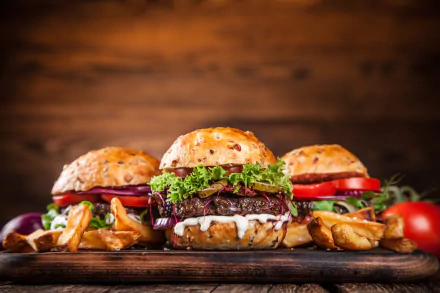 HD desktop wallpaper featuring three juicy burgers with lettuce, tomato, and crispy fries on a wooden surface against a warm, rustic background.