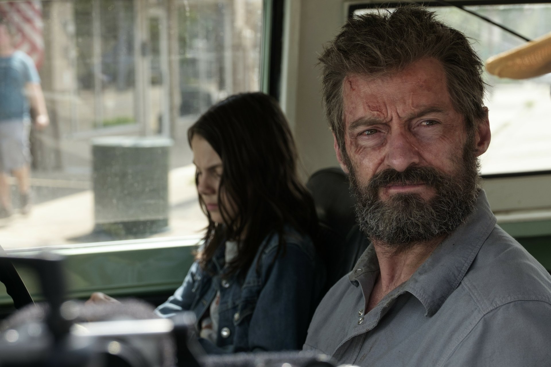 A scene from the movie Logan featuring X-23 (Laura Kinney) and Wolverine (Hugh Jackman). The characters are in a car, with Laura looking down and Logan staring outward. HD desktop wallpaper.