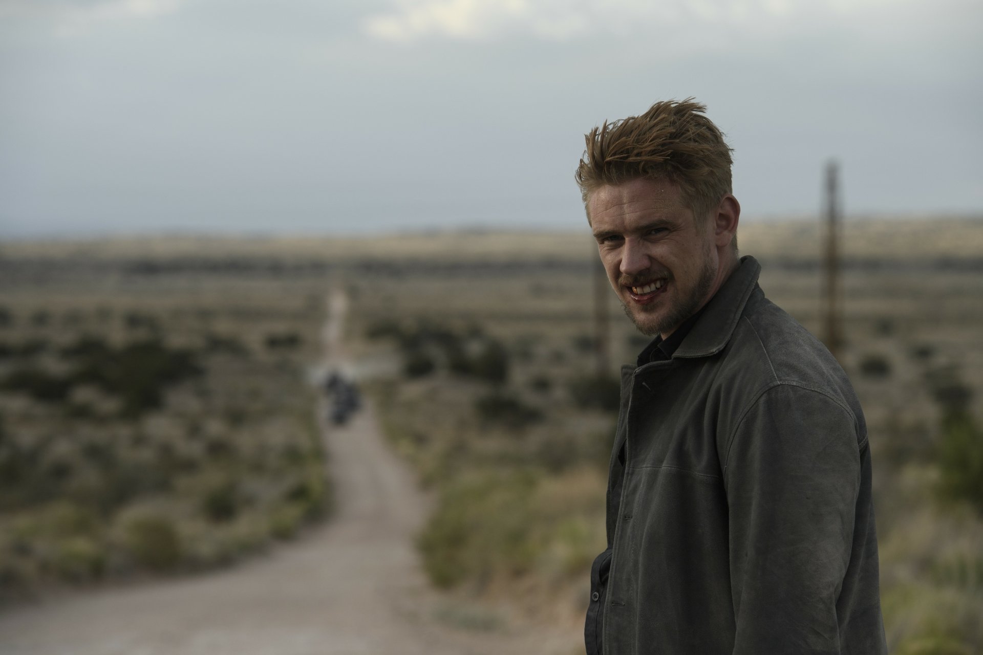 HD desktop wallpaper featuring Boyd Holbrook in a scene from the movie Logan, set against a vast, arid landscape with a dirt road stretching into the distance.
