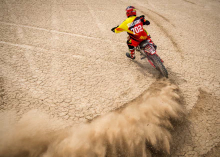 A motocross rider kicks up dust while making a sharp turn on a dry track, showcasing the excitement and intensity of sports in this dynamic HD desktop wallpaper.