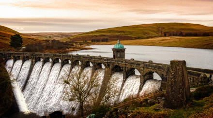 HD landscape wallpaper showing a man-made dam with water flowing into a lake, set against rolling hills under a soft, colorful sky.